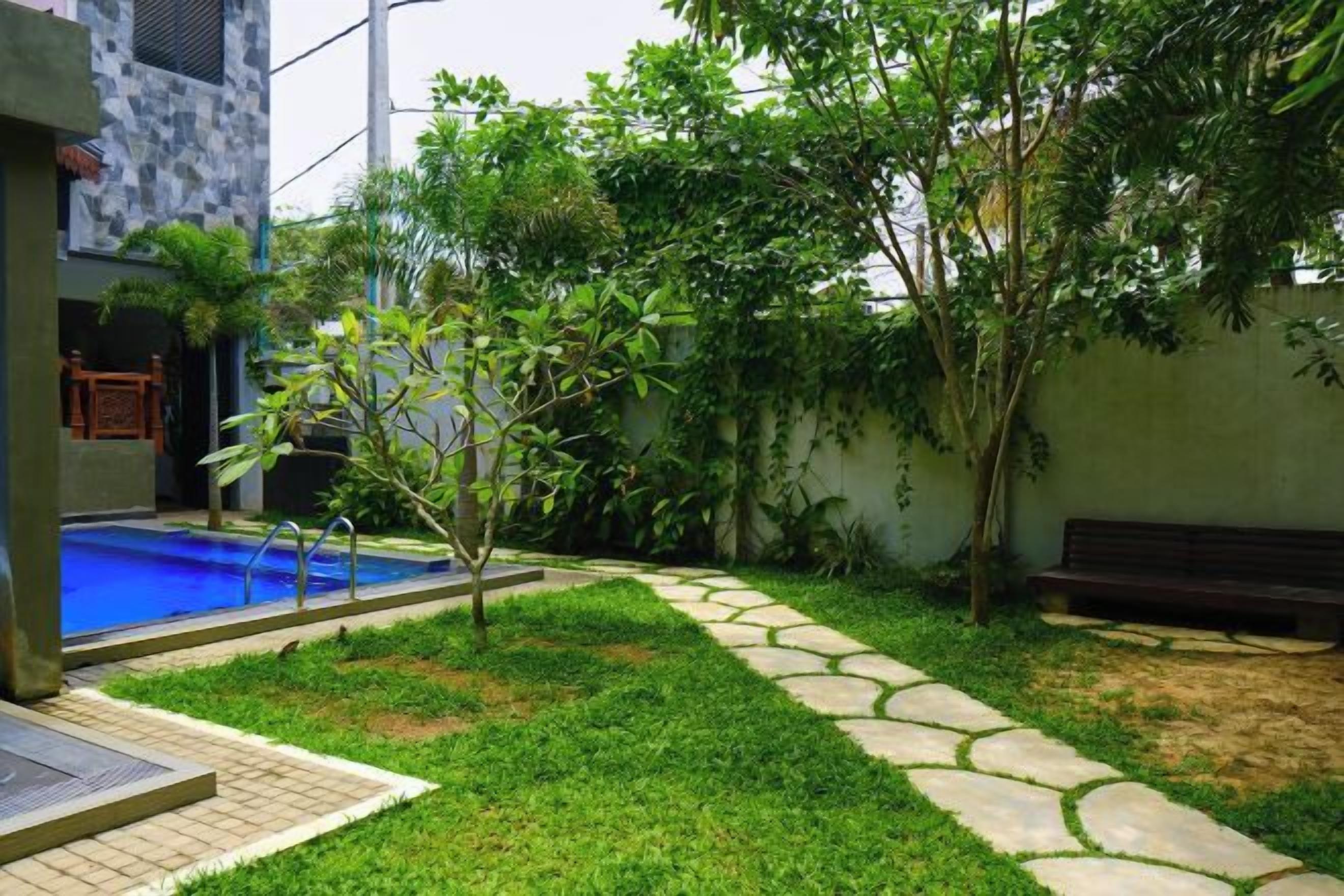 Un patio trasero residencial con piscina, un sendero de piedra y un banco.