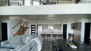 A spacious living area with a large gray sectional sofa, a dining table with chairs, and a kitchen in the background.