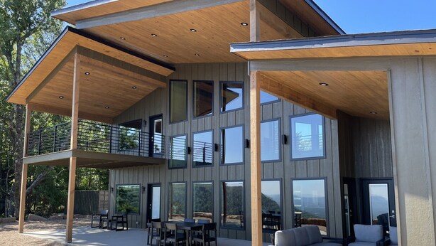 A modern two-story house with a covered patio area featuring outdoor furniture.