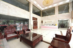 A spacious lobby with traditional wooden furniture, a large reception desk, and a view of the street through large windows. - Junyu Hotel (Guangdong Women's Vocational and Technical College Asian Games Village Branch) (Guangzhou)
