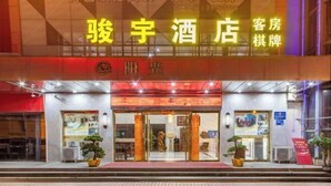 A hotel entrance with a neon sign, glass doors, and potted plants. - Junyu Hotel (Guangdong Women's Vocational and Technical College Asian Games Village Branch) (Guangzhou)