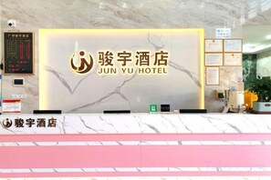 A reception desk with a sign for Jun Yu Hotel, a control panel, and a wall with framed notices. - Junyu Hotel (Guangdong Women's Vocational and Technical College Asian Games Village Branch) (Guangzhou)