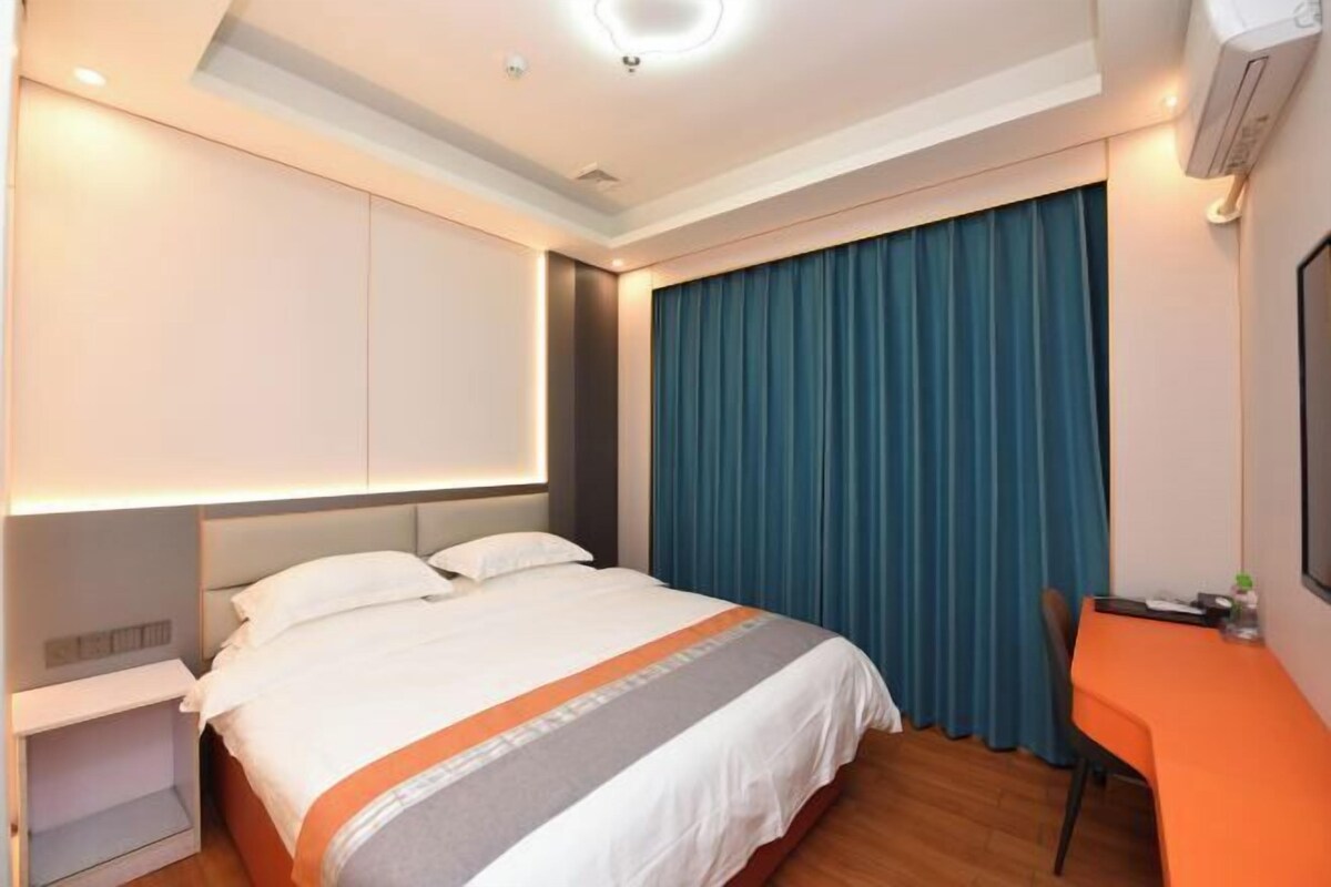 A hotel room with a bed, a desk, and a window with curtains.