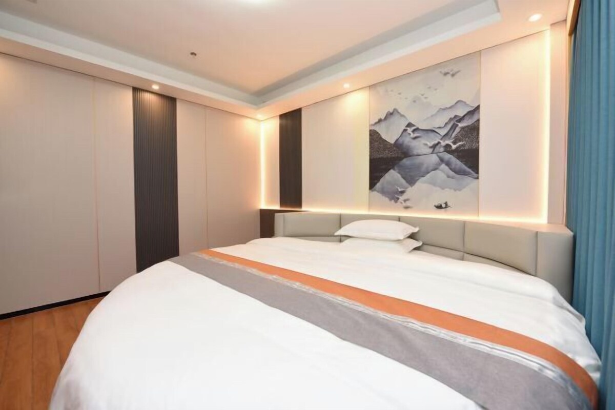 A modern hotel room with a large bed, a wall-mounted artwork, and built-in wardrobes.