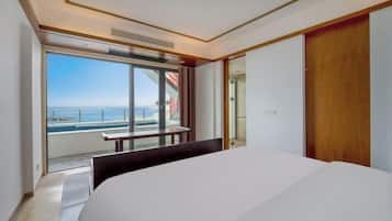 Ein modernes Hotelzimmer mit einem großen Bett, einer Schiebetür zu einem Balkon mit Meerblick und einem Holzschrank.