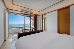 A modern hotel room with a large bed, a sliding glass door leading to a balcony with a view of the sea, and a wooden wardrobe. - Xunliao Bay Yijing Holiday Sea-view Hotel (Huidong)