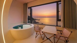 Un balcón con vista al mar al atardecer, un jacuzzi y una mesa con sillas.