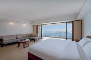 A hotel room with a large bed, a sofa, a small table, and a balcony with a view of the sea. - Xunliao Bay Yijing Holiday Sea-view Hotel (Huidong)