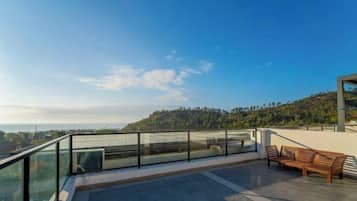 Eine moderne Terrasse im Freien mit Glasgeländer, einer Holzbank und Blick auf eine hügelige Landschaft.