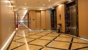 A hotel corridor with a patterned floor, elevators, and a fire extinguisher.