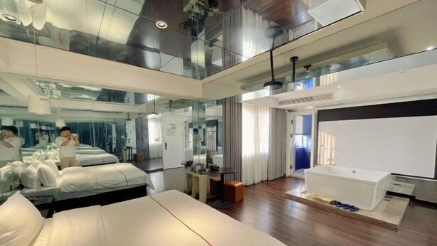 A modern hotel room with a large bed, a separate bathroom with a bathtub, and a glass-enclosed balcony.