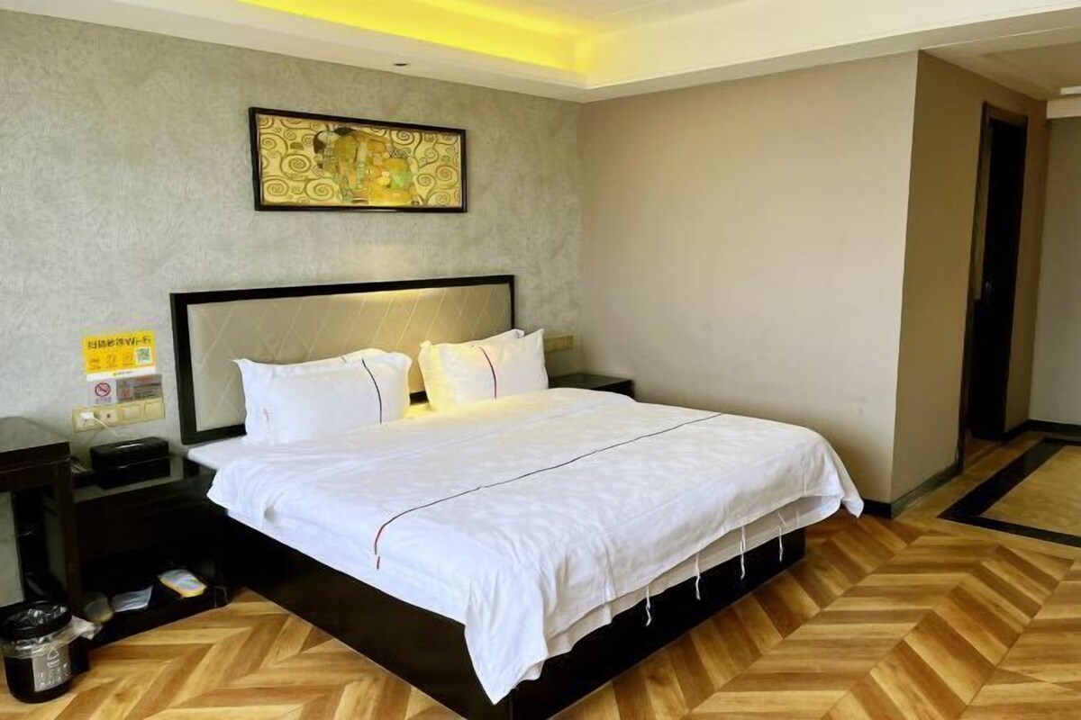 Ein Hotelzimmer mit einem großen Bett, einem Nachttisch, einer Mülleimer und einem Wandbild.