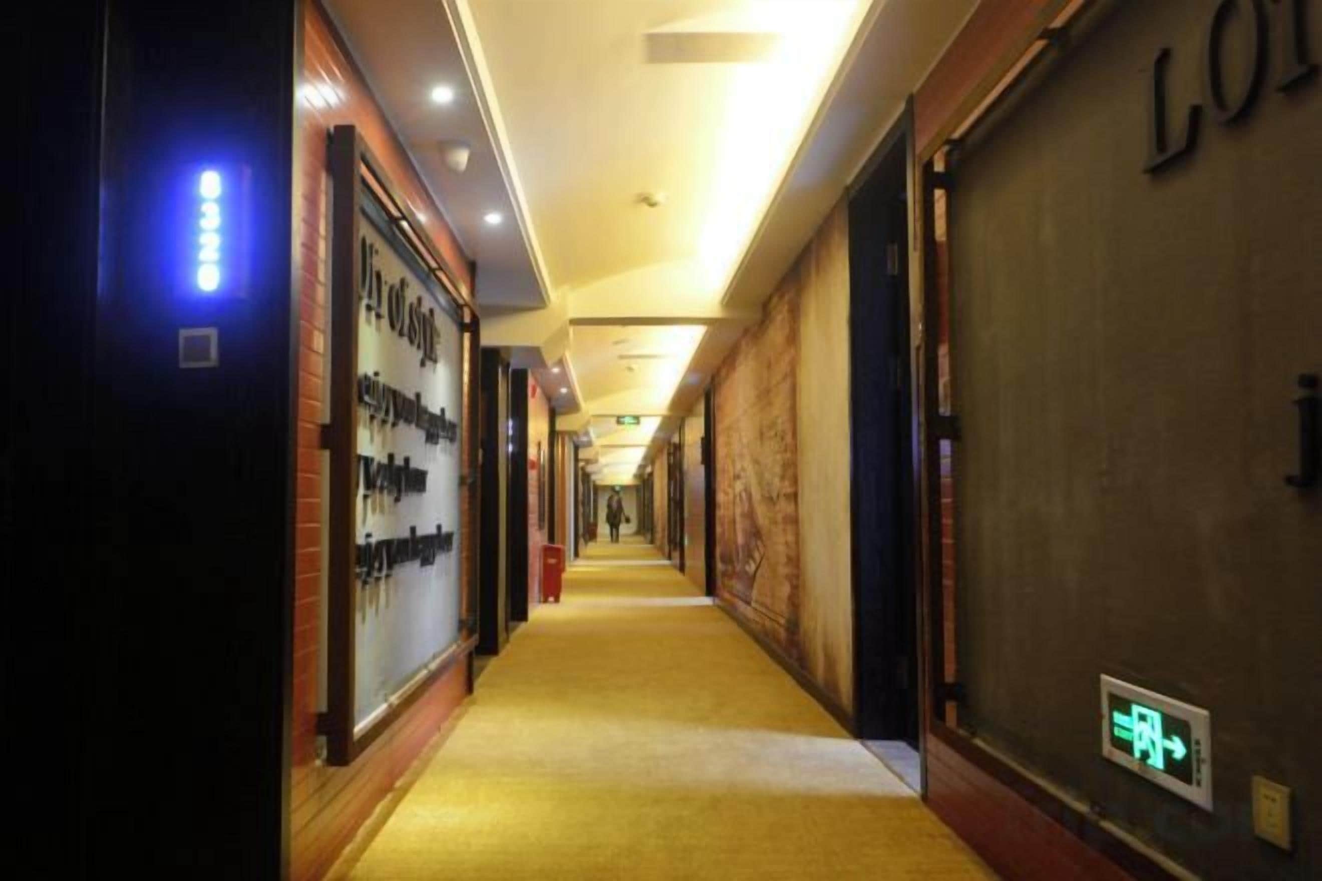 A hotel corridor with a carpeted floor, illuminated by overhead lights, and a sign indicating the exit.