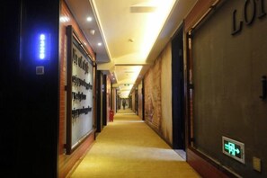 Pasillo de hotel con piso alfombrado, iluminado por luces en el techo y un letrero que indica la salida.