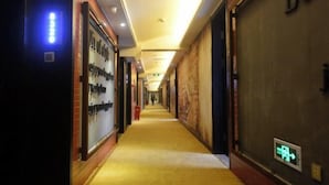A hotel corridor with a carpeted floor, illuminated by ceiling lights, and a visible exit sign.