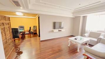 A hotel room with a wooden floor, a white sofa, a white armchair, a small white table, and a TV mounted on the wall.