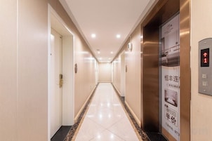 Un pasillo de hotel con piso de mármol, puertas a la izquierda y un ascensor a la derecha.