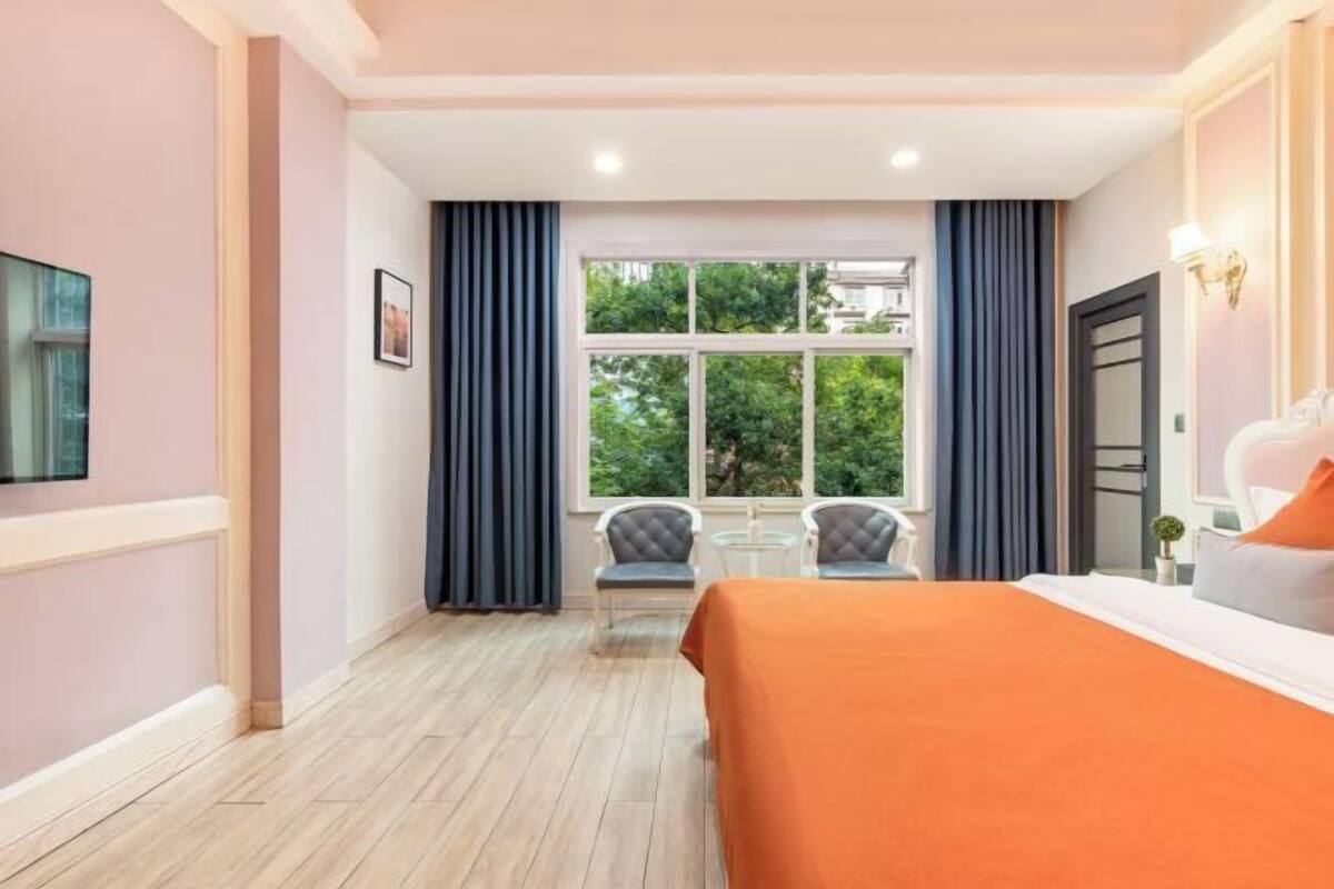 Una habitación de hotel con una cama grande, una ventana con cortinas, una mesita pequeña y una silla.