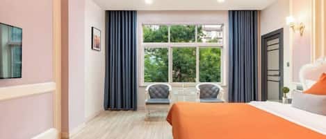 A hotel room with a large bed, a window with curtains, a small table, and a chair.