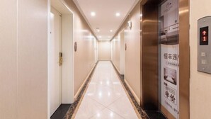 A hotel hallway with a tiled floor, doors on the left, and an elevator on the right.