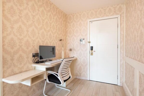 Um quarto pequeno com uma escrivaninha, uma cadeira, uma televisão e uma porta.