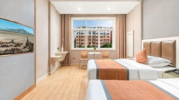 A hotel room with two beds, a desk, a chair, and a large window with a view of a building.