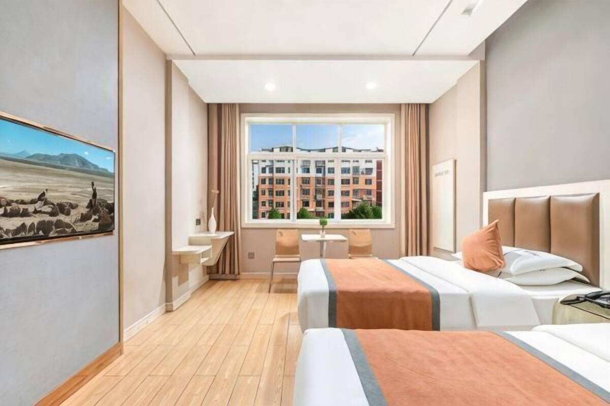 Habitación de hotel con dos camas, un escritorio, una silla y un ventanal con vistas a un edificio.