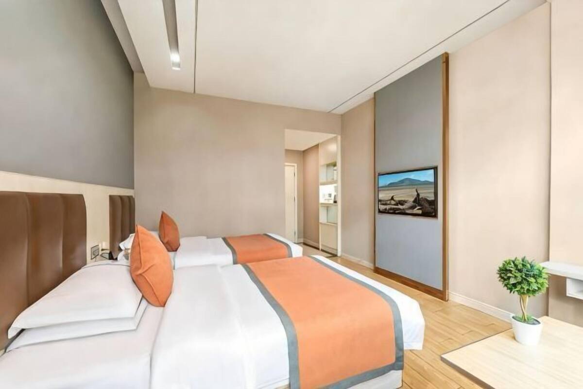 Una habitación de hotel con dos camas, una mesita pequeña, una planta en maceta y un cuadro en la pared.
