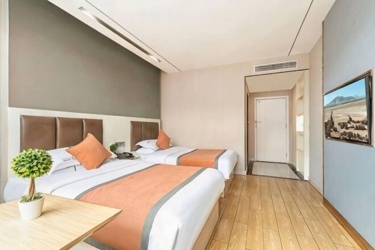 Habitación de hotel con dos camas, piso de madera, una mesita con una planta y un cuadro en la pared.