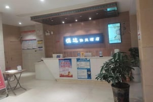 A reception desk with a digital display, informational posters, and a potted plant.