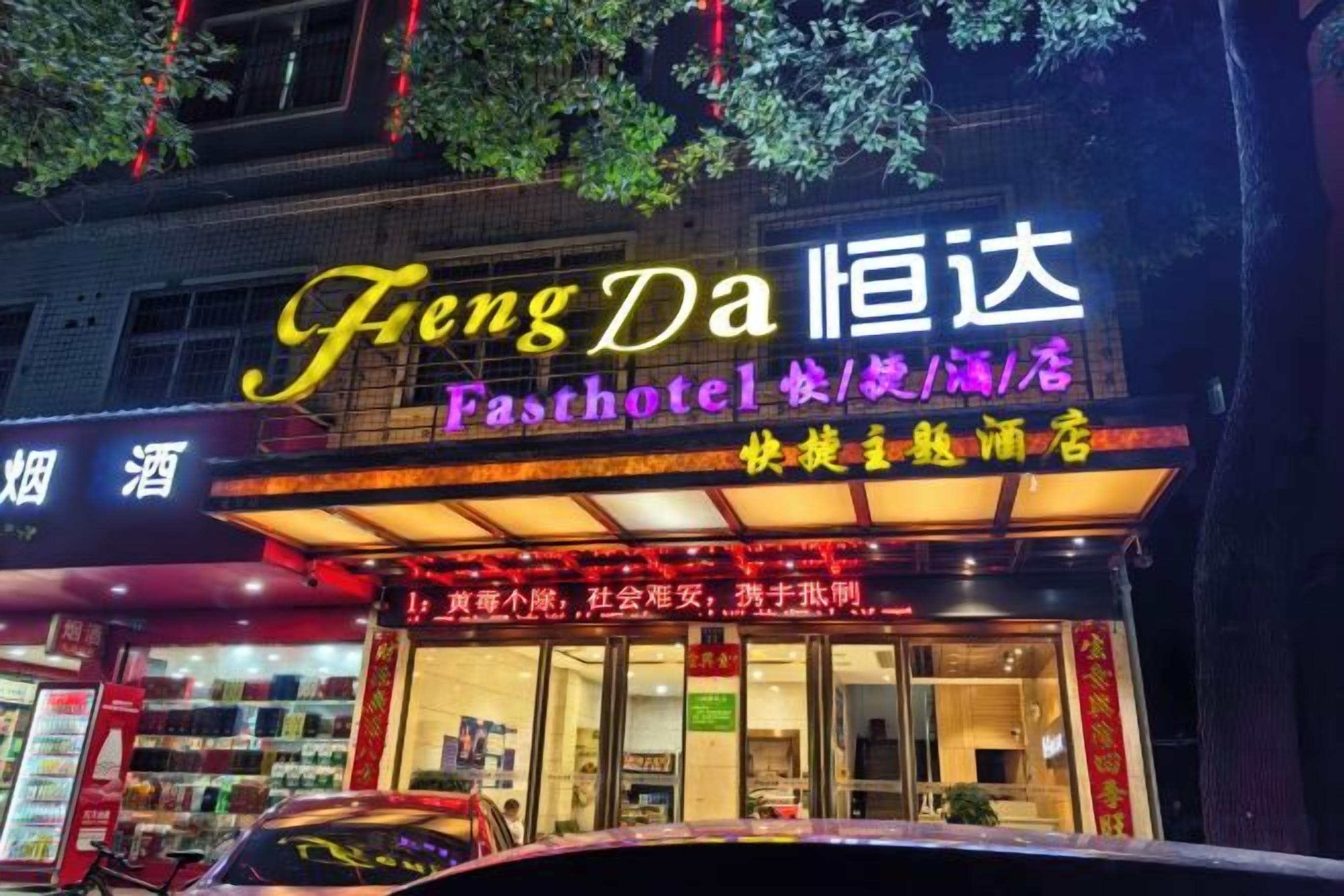 A hotel with a neon sign, a storefront with a glass facade, and a car parked in front.