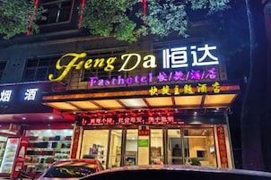 A hotel with a neon sign, a storefront with a glass facade, and a car parked in front.