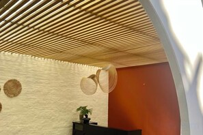 Et værelse med en lægtepanelloft, en hvid væg med struktur og en mørk receptionsdisk med en plante.