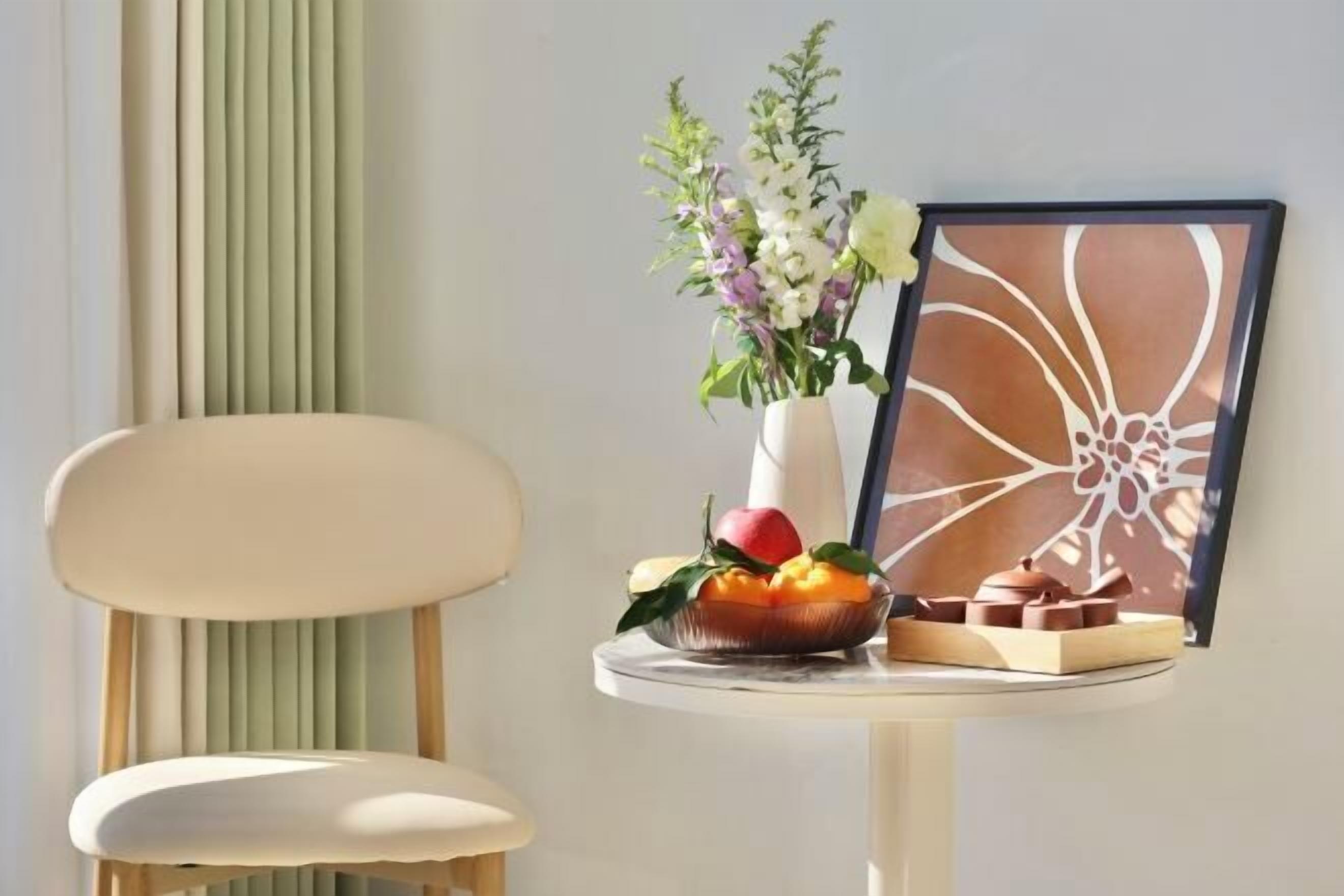 Una mesa con un jarrón de flores, un frutero y un cuadro enmarcado.