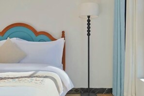 Cama bem arrumada com cabeceira de madeira, luminária de chão e cortinas azul-claras.