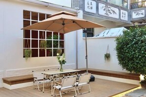 Un patio al aire libre con una mesa, sillas, una planta colgante y un paraguas grande.