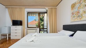 A hotel room with a bed, a TV, a desk with a computer, and a window with curtains.