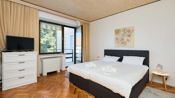 A modern hotel room with a large bed, a television on a dresser, and a window with curtains.