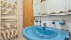 A bathroom with a blue sink, white tiled walls, a wooden door, and a towel rack.