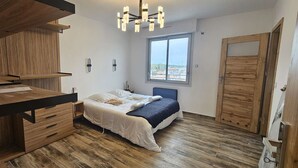 Un dormitorio con un escritorio de madera, una cama con cabecera azul y un ventanal grande.
