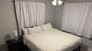 Una cama bien hecha con ropa blanca, una mesita de noche con lámpara y un ventilador de techo.