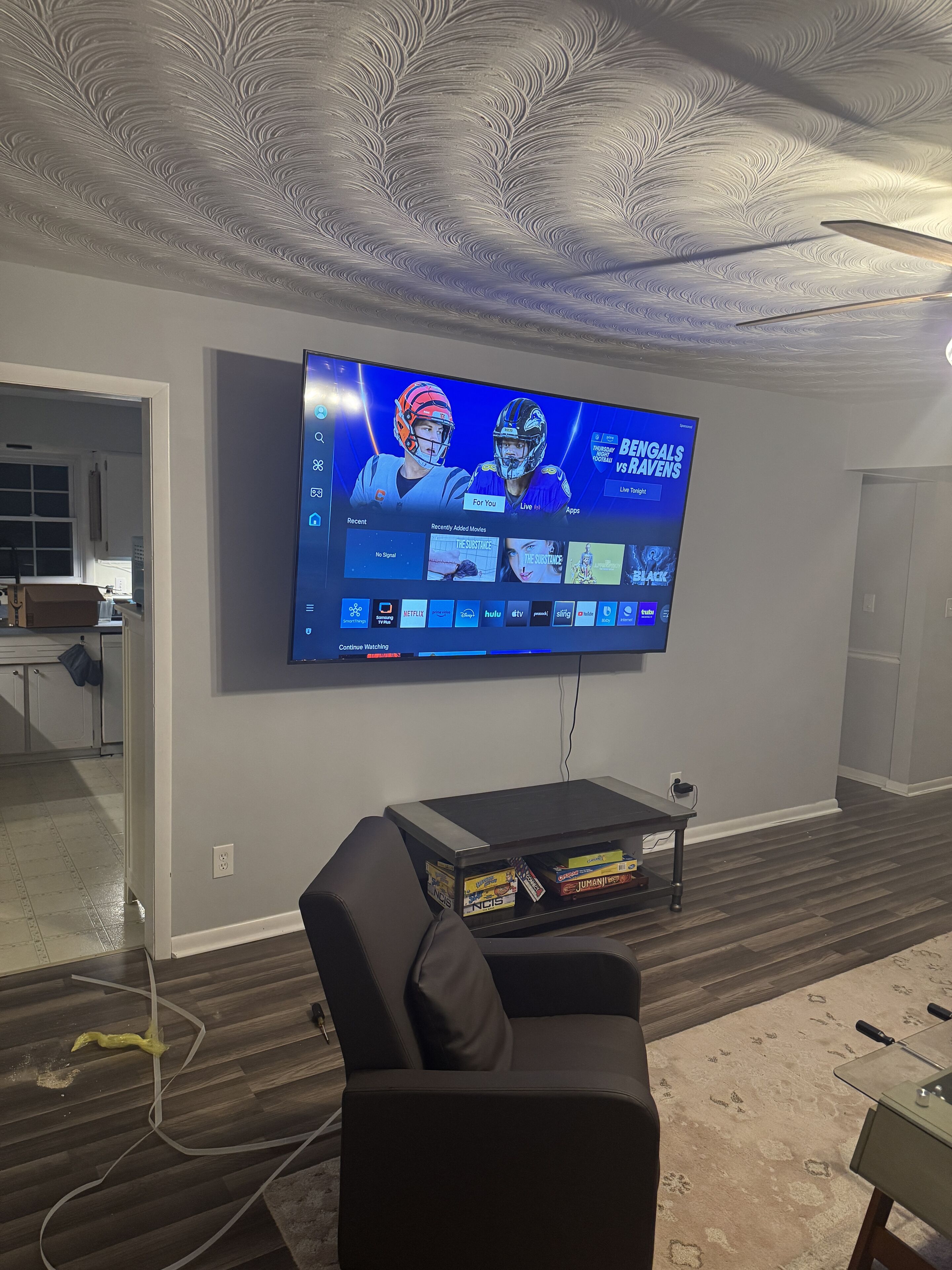 A living room with a flat-screen TV mounted on the wall, a dark leather couch, and a coffee table with game cases.