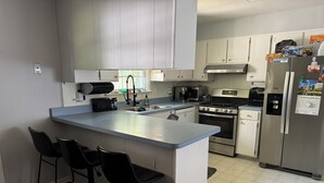 Una cocina moderna con una isla central, taburetes de bar, electrodomésticos de acero inoxidable y armarios de tonos claros.