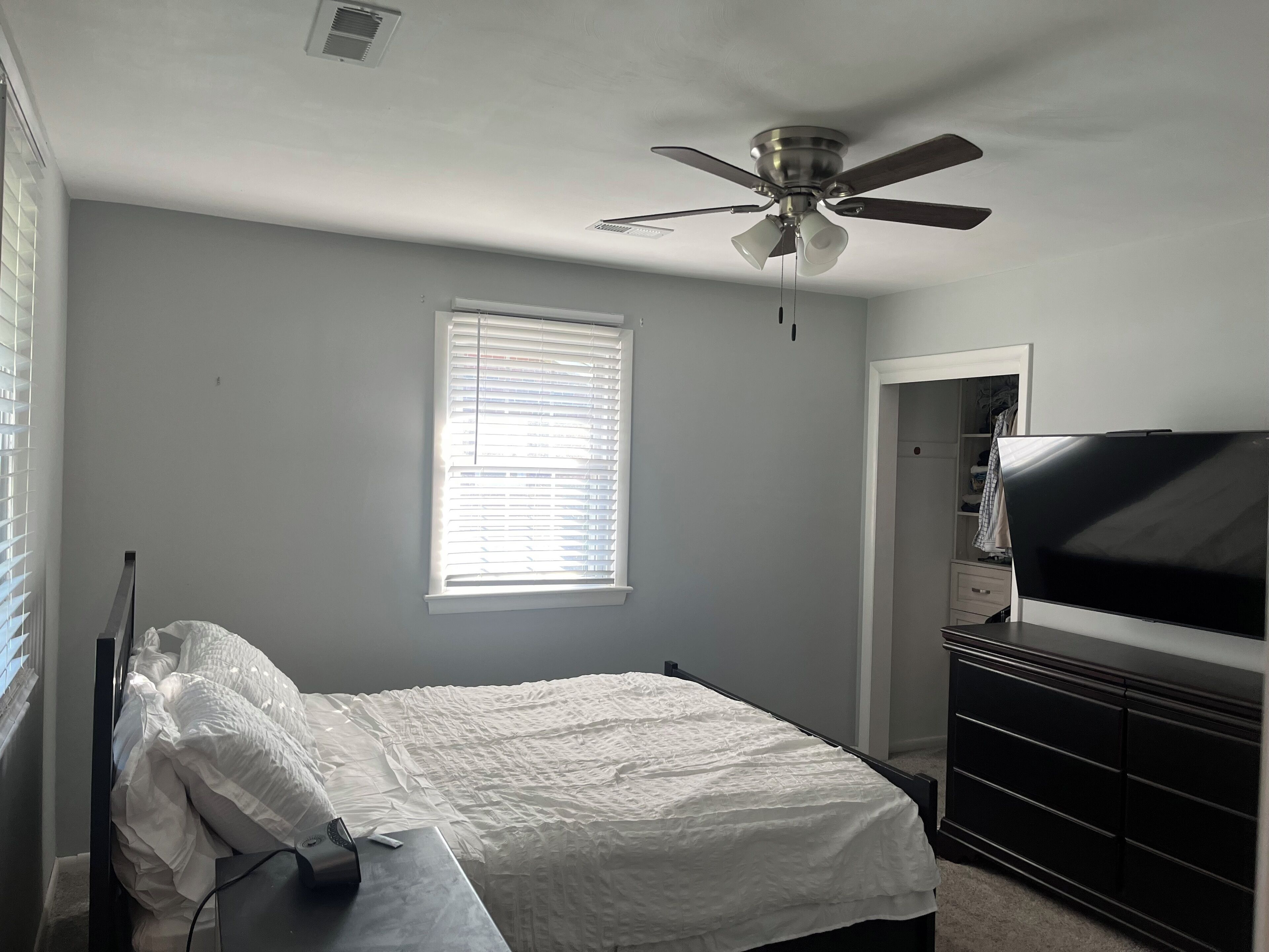 A bedroom with a bed, a ceiling fan, a TV, and a dresser.
