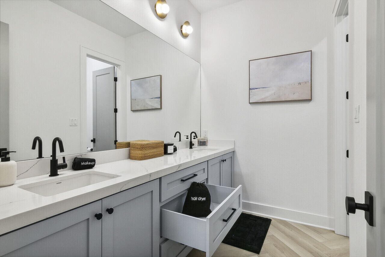 A modern bathroom with a white vanity, a large mirror, and a hair dryer in the drawer.