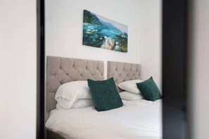 Ein Schlafzimmer mit einer gesteppten Kopfteil, weißer Bettwäsche und zwei grünen Kissen.