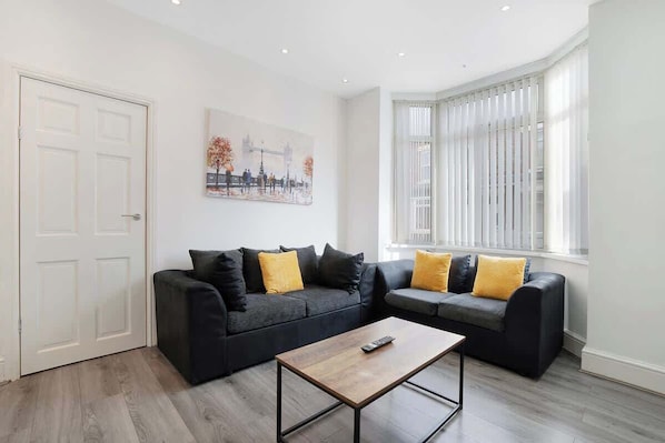 Ein stilvolles Wohnzimmer mit einer schwarzen Sofagarnitur, einem Holztisch und einem Stadtbild an der Wand.