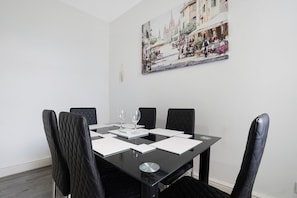 Ein Esszimmer mit einem schwarzen Tisch, vier Stühlen und einem Gemälde einer Straßenszene an der Wand.