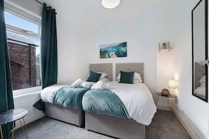 Une chambre à coucher avec un lit, une table de chevet, une lampe, un tableau au mur et une fenêtre avec des rideaux.