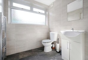 Une salle de bain avec des toilettes, un lavabo, un miroir et une fenêtre.